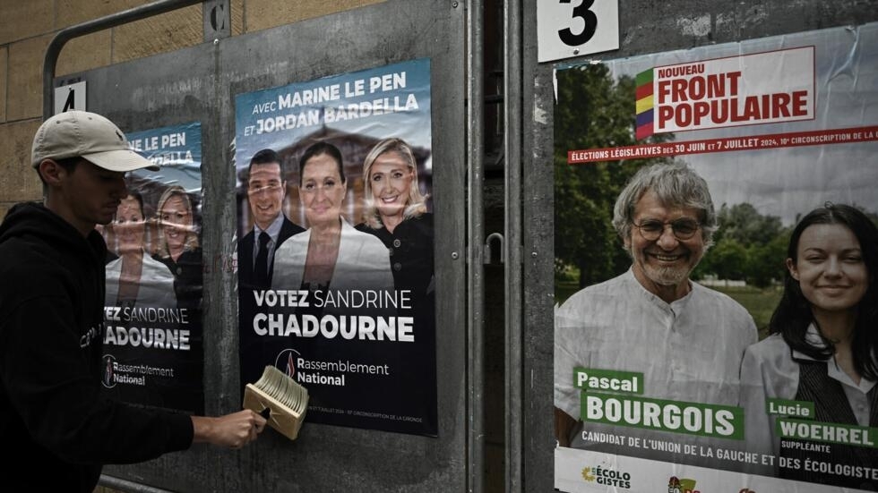 Un militant colle une affiche électorale de la candidate d'extrême droite du Rassemblement national (RN), Sandrine Chadournec (C), aux côtés du candidat opposant du Nouveau Front populaire, Pascal Bourgois, à Libourne, dans le sud-ouest de la France, le 2 juillet 2024, dans le cadre des élections législatives françaises.