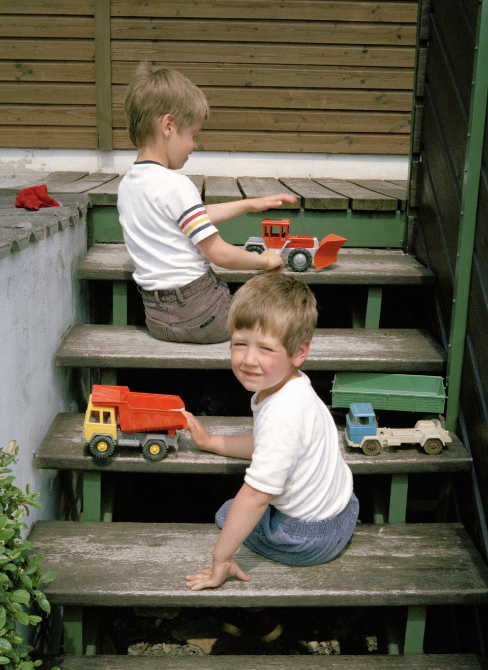 Two children are playing with toy trucks on wooden outdoor stairs