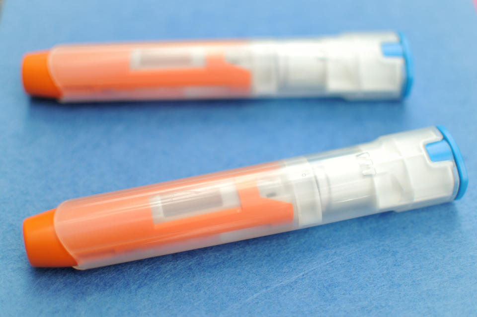 Two EpiPen auto-injectors are placed on a solid blue background