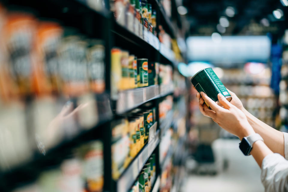 Knowing how to read a label on canned foods is essential in making informed decisions. (via Getty Images) Close up of a woman grocery shopping in supermarket. Holding a tin can and reading the nutrition label at the back