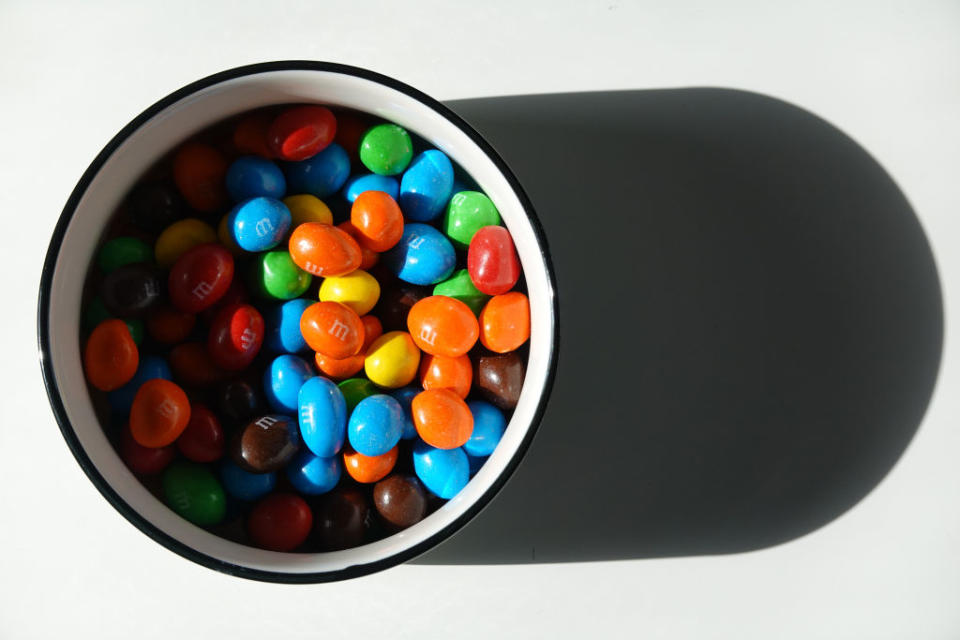 A white bowl filled with colorful M&M candies sits on a surface, casting a shadow to the right