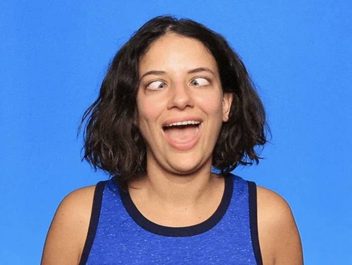 A person in a sleeveless top is making a funny face by crossing their eyes and smiling. The background is plain. The person is not identified
