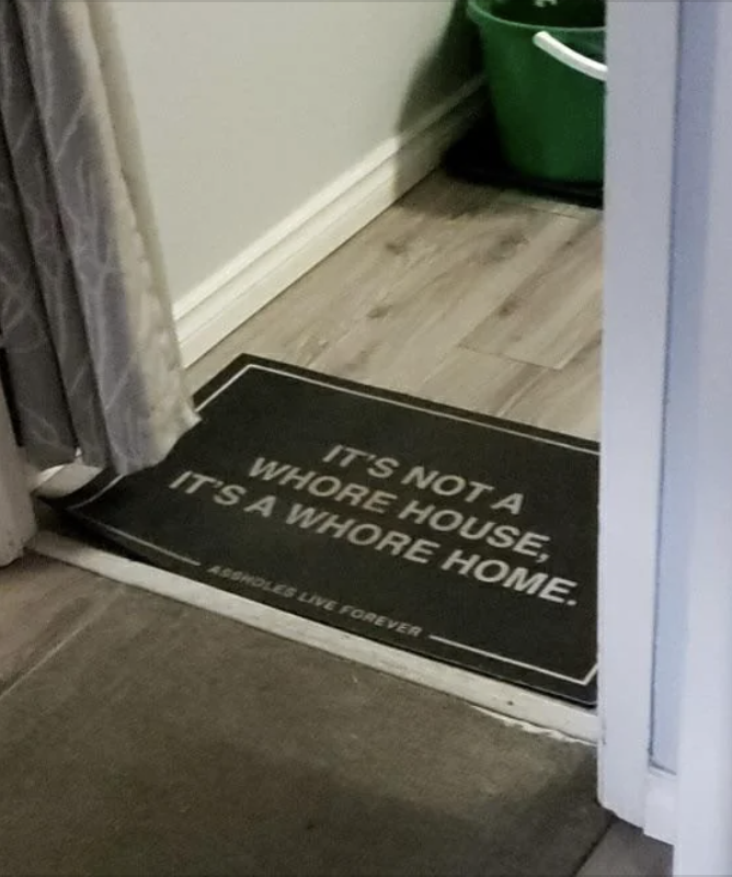 Doormat at the entrance of a home with the text: "IT'S NOT A WHORE HOUSE, IT'S A WHORE HOME. ASSHOLES LIVE FOREVER."