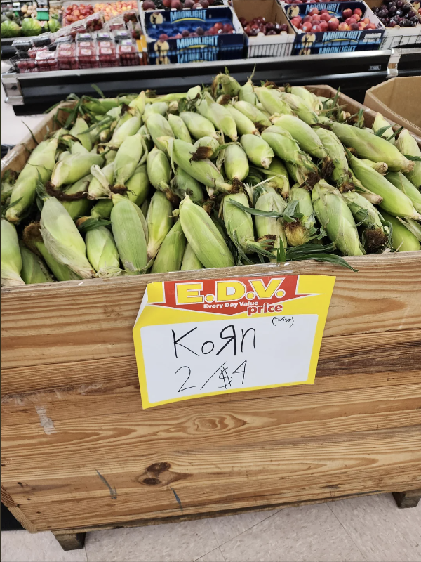 A grocery store display of fresh corn with a sign reading "Korn, 2 for $4."