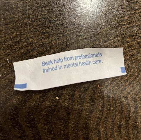 Fortune cookie paper on a wooden table that reads: "Seek help from professionals trained in mental health care."