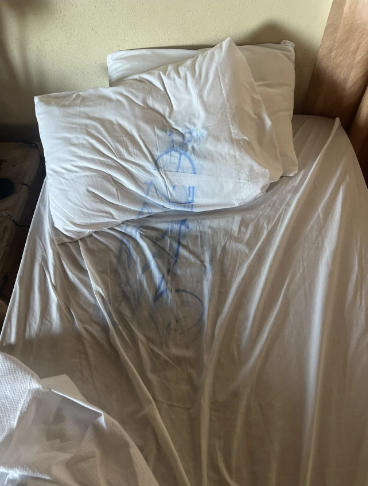 Unmade bed with pillows, sheet has a blue ink drawing of a bike