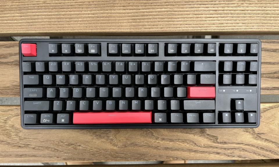 The Keychron C3 Pro mechanical keyboard in black and red, resting on a brown wooden outdoor tablet.
