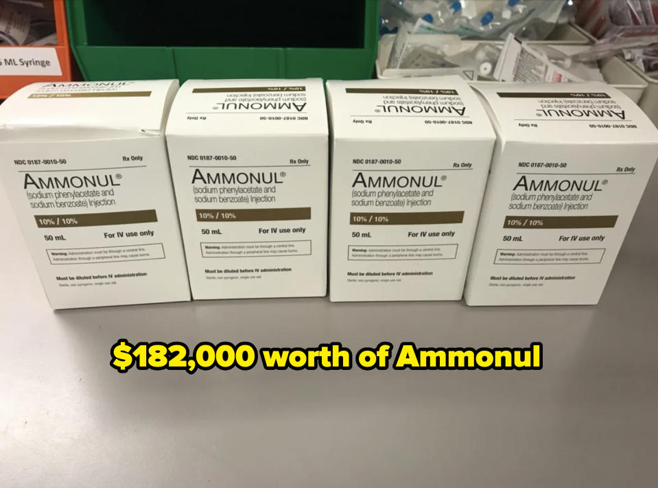 Four boxes of Ammonul, a sodium phenylacetate and sodium benzoate injection medication. The boxes are aligned on a grey surface in a medical setting