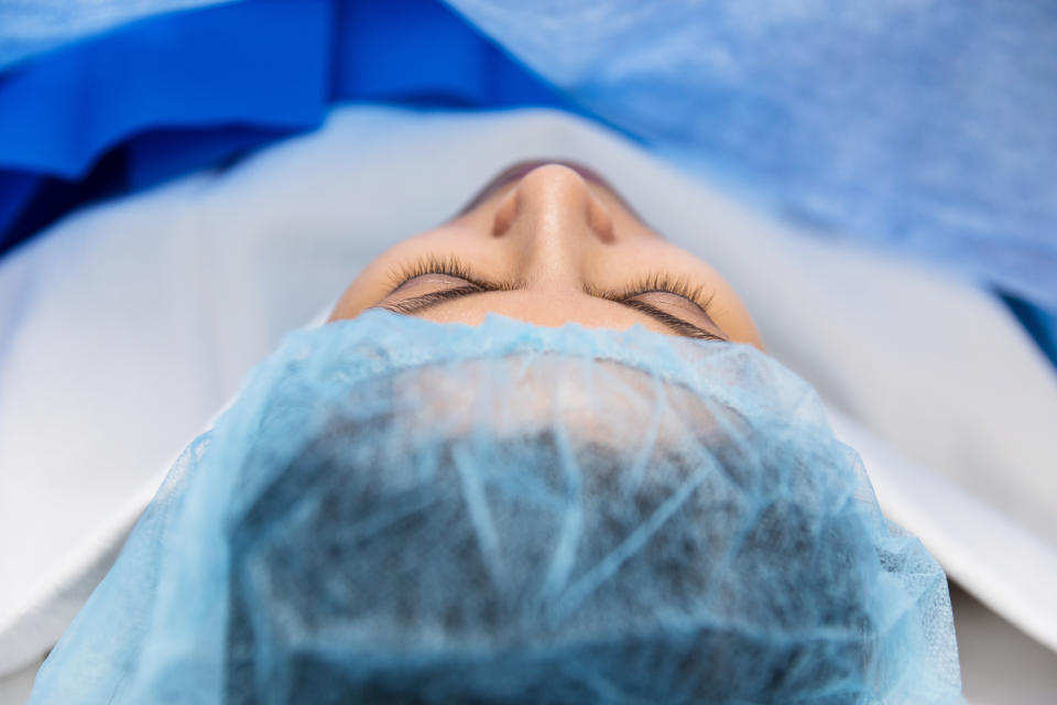 A person lies under a blue surgical drape, with their eyes closed, possibly undergoing or preparing for a medical procedure