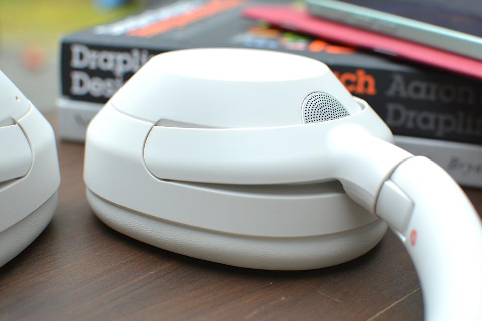 <p>Headband and ear cup detail of a set of white headphones showing speaker grille design.</p>
