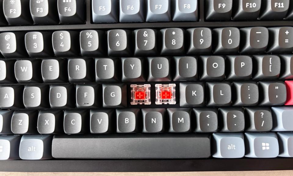A close-up of a gaming keyboard with two keycaps removed, displaying the 