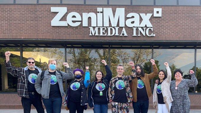 2023 photo of ZeniMax workers standing in a line, raising their fists in unison in front of a ZeniMax Media office.