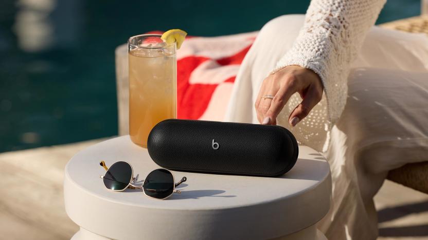 A black Beats Pill speaker on a small outdoor table with sunglasses and an iced beverage. 