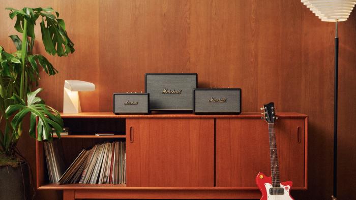 A living room media console has three Marshall speakers on it, with records in the cabinet and a guitar leaning against it.