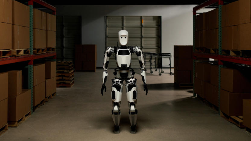 A white and black android stands in a shadowy warehouse corridor, facing the camera.