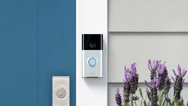 A Ring doorbell camera mounted on the frame of a blue door next to some flowers.