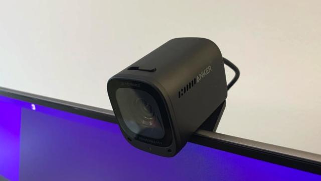 Photo of the Anker PowerConf C200 webcam (closeup, left side view) mounted on top of a monitor with purple on its screen.