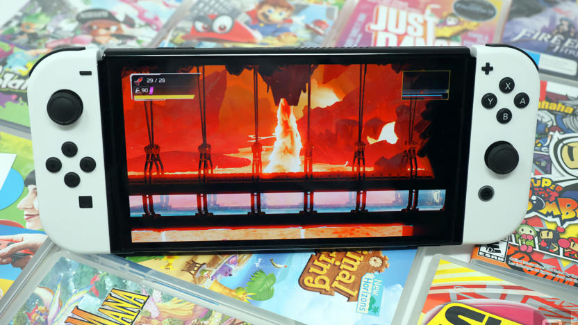 Photo of the Nintendo Switch OLED sitting on a colorful array of game cartridge cases. Its screen shows a fiery scene.