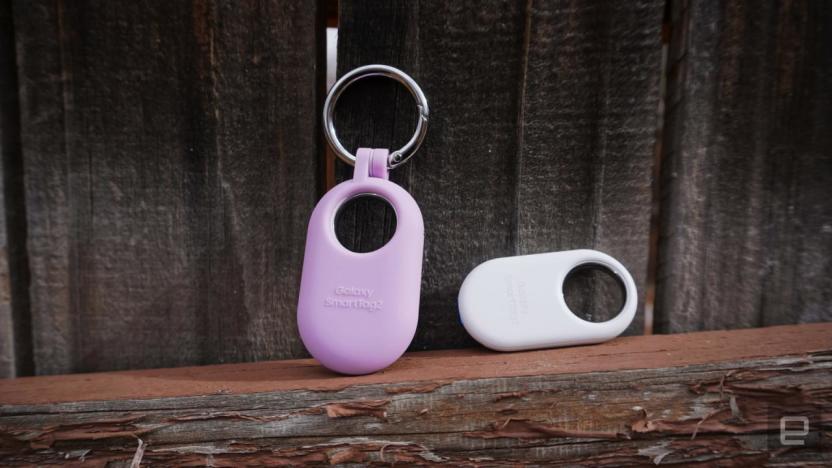 Two Samsung Galaxy SmartTag 2 Bluetooth trackers sit against a wood backdrop, one pink and the other white.
