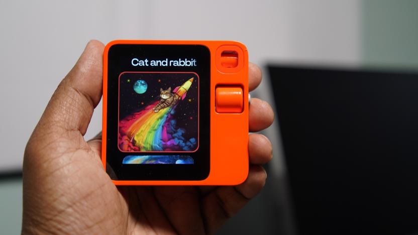 A hand holding a small square orange device with a display.