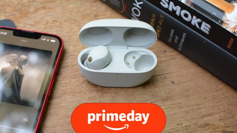 The Sony WF-1000XM5 earbuds are on a wooden table with books nearby along with a phone displaying an album cover. The prime day logo is at the bottom of the image. 