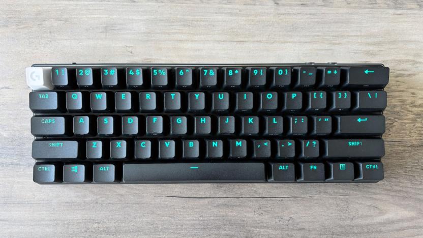 The Logitech G Pro X 60 wireless gaming keyboard in black sits on a wooden tabletop with light blue RGB backlighting displayed through its keycaps.