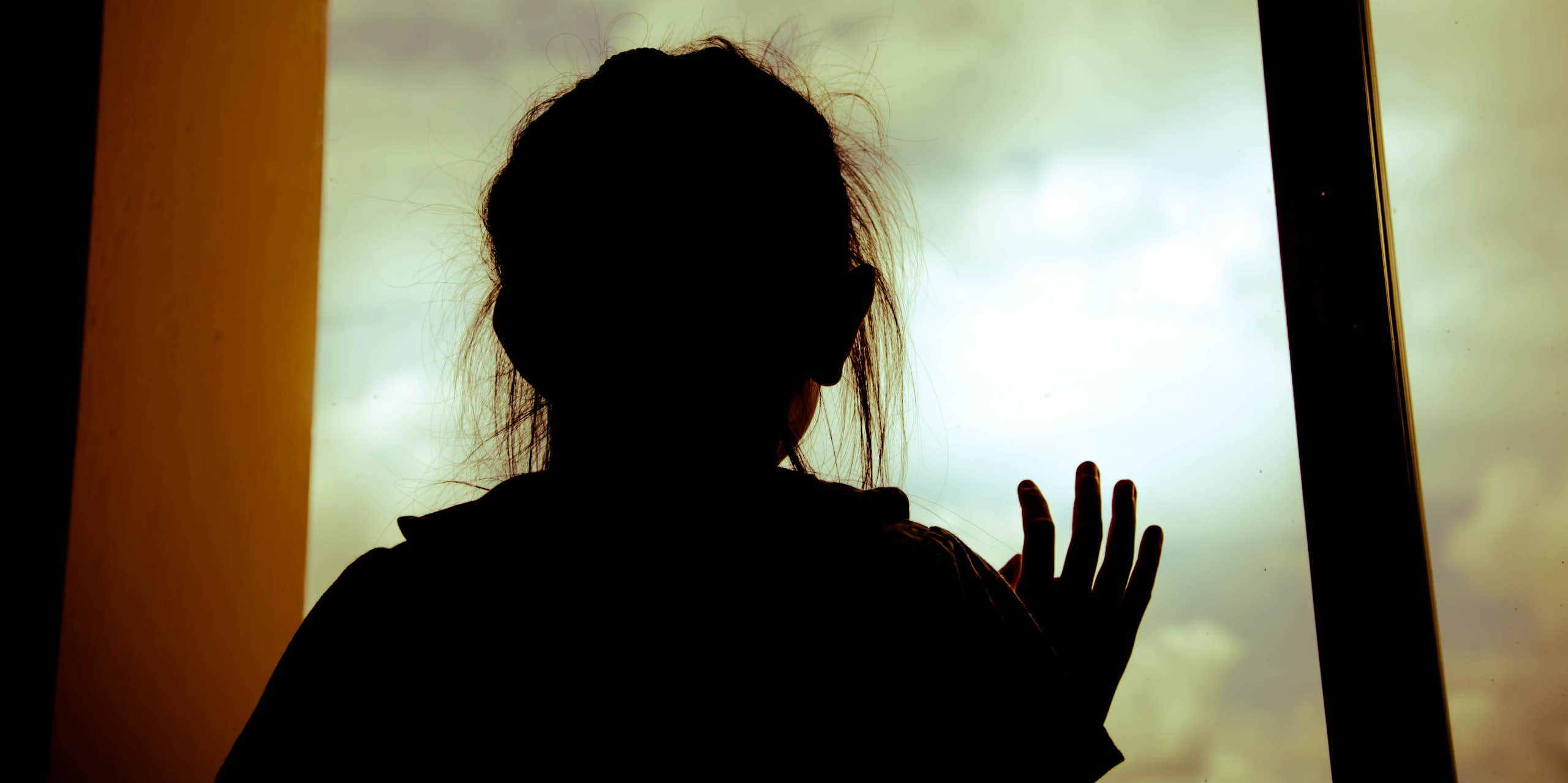 Silhouette sad little girl in room and looking out the window